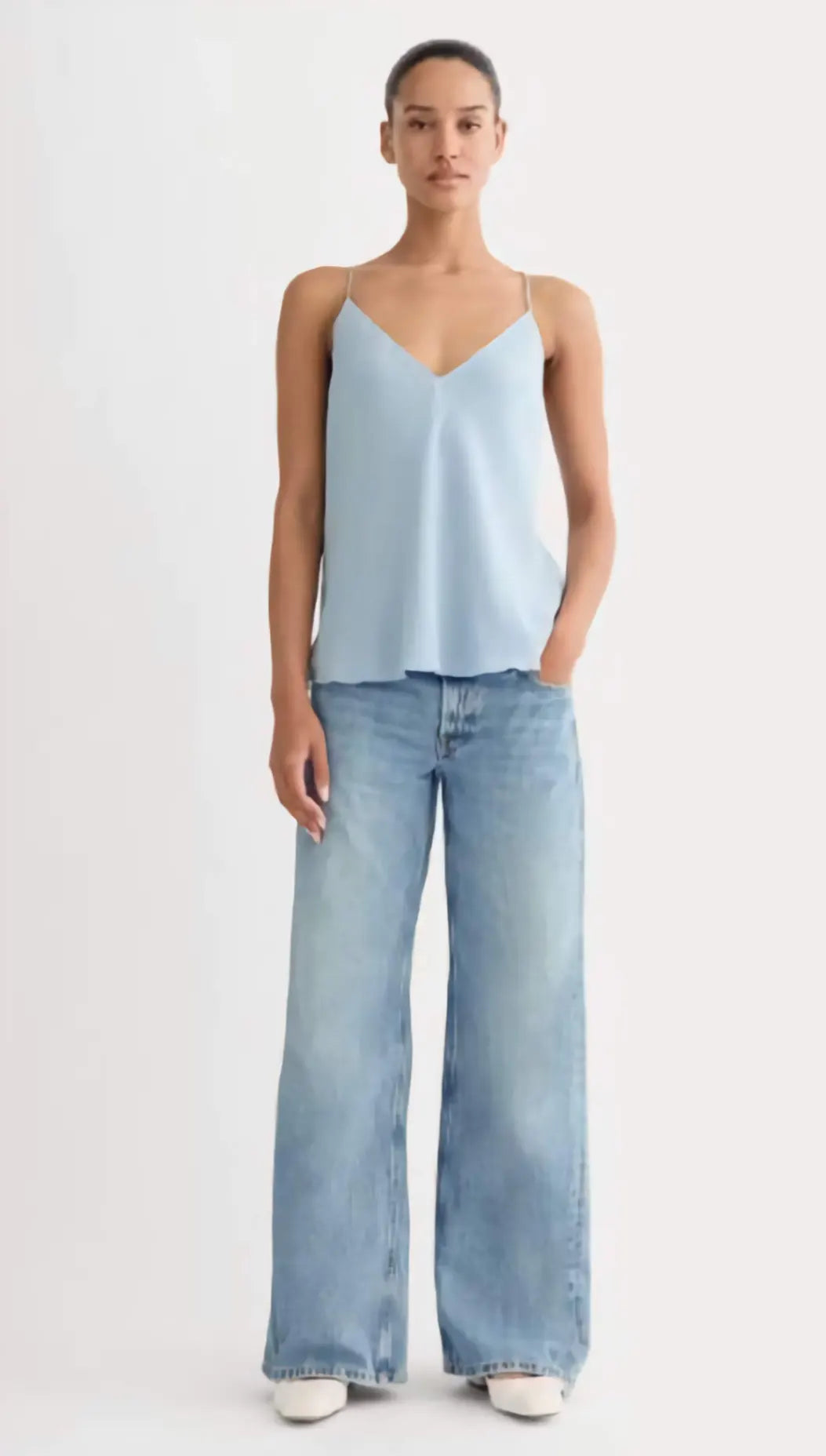 Woman wearing a light blue sleeveless top and wide-leg jeans on a white background