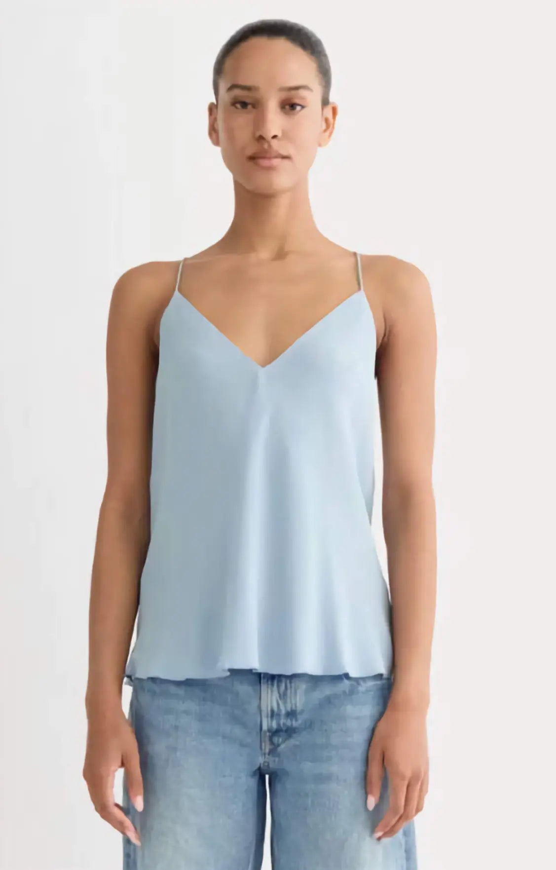 Woman wearing a light blue spaghetti strap top and jeans on a white background