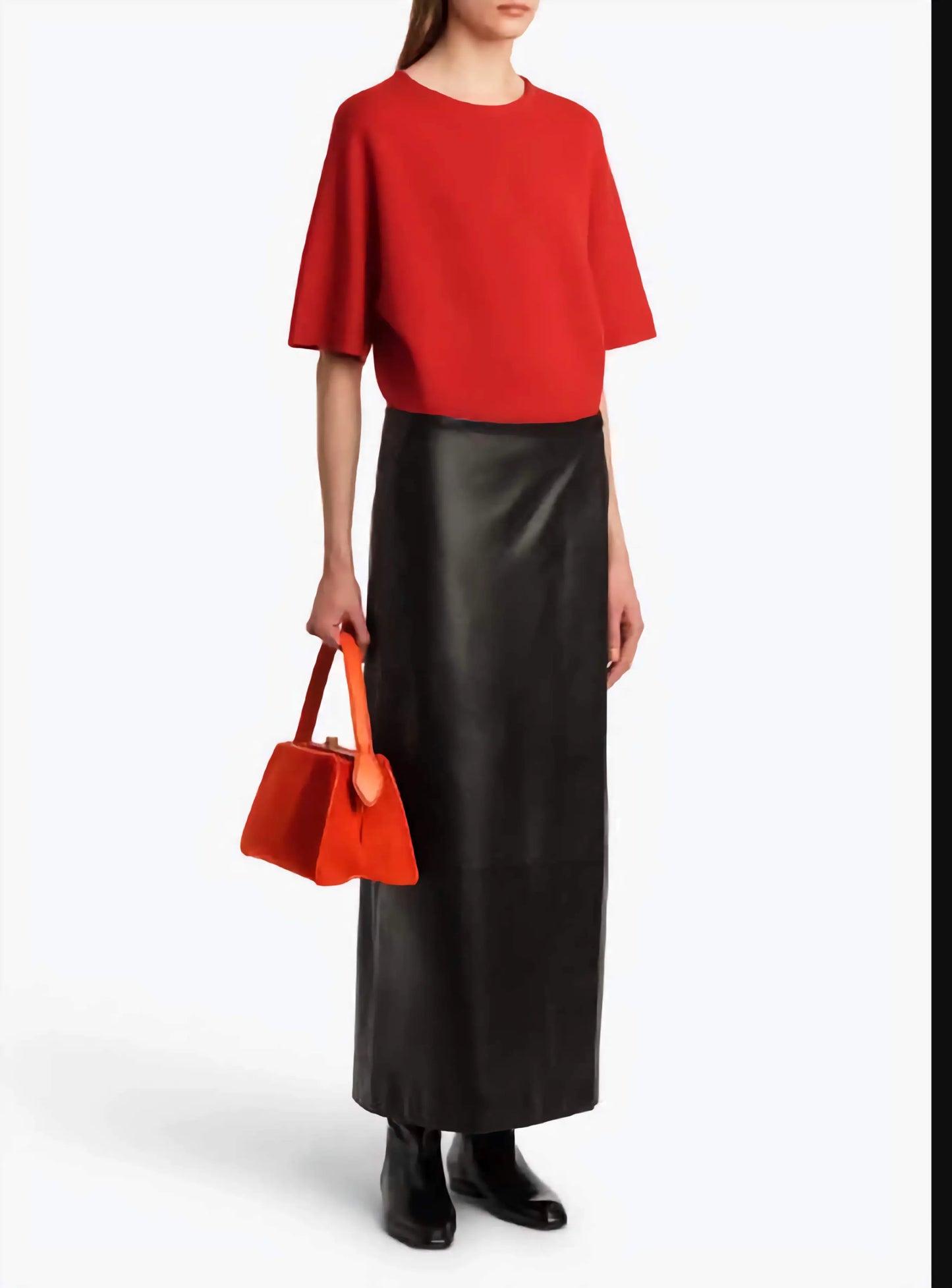 Person wearing a red top and black skirt holding an orange handbag on a white background
