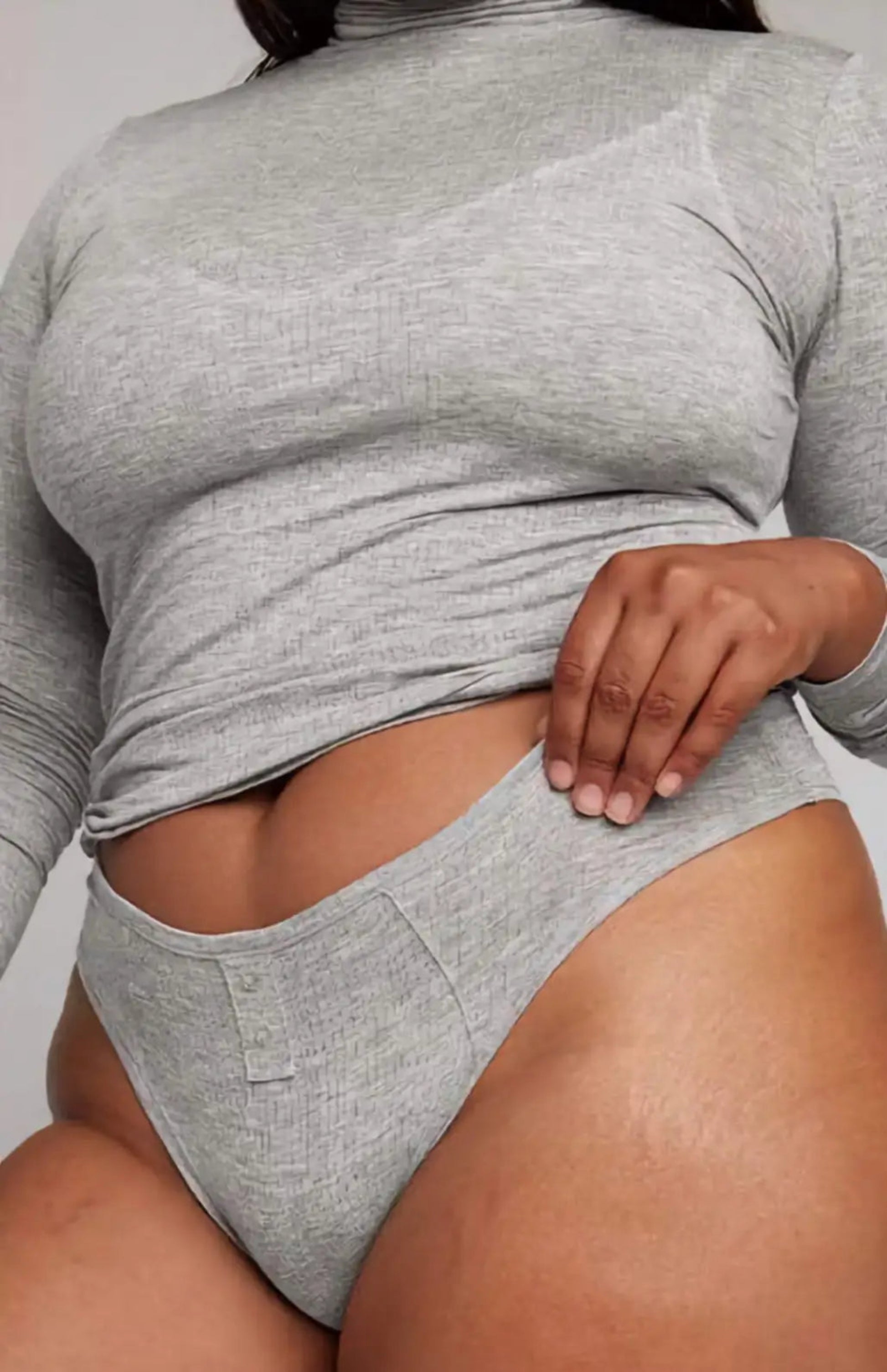 Person wearing a gray long-sleeve top and matching underwear set against a neutral background