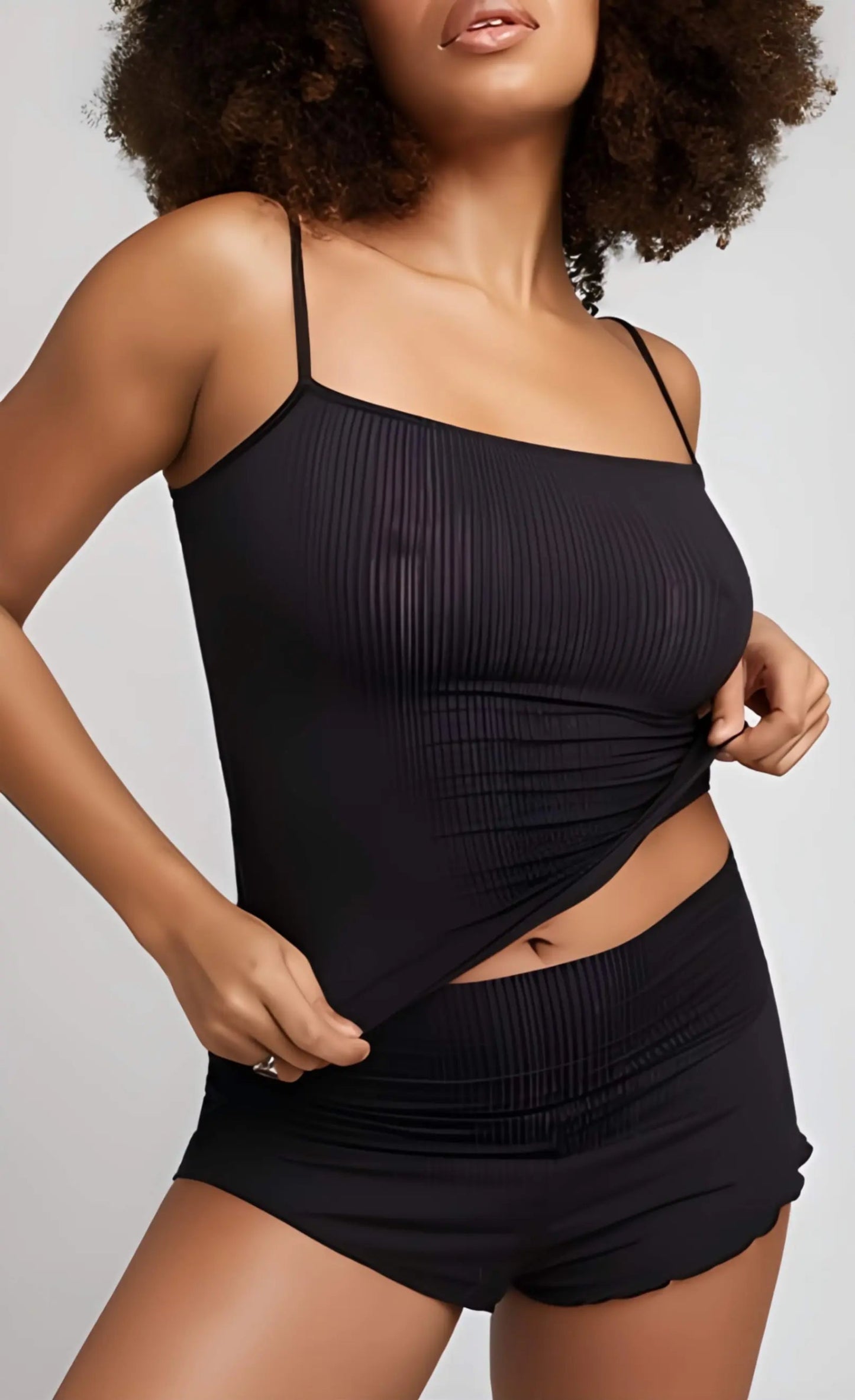 Woman wearing a black ribbed tank top and shorts on a gray background