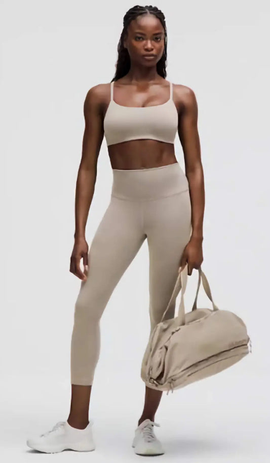 Woman in beige athletic outfit holding a matching duffel bag on a white background