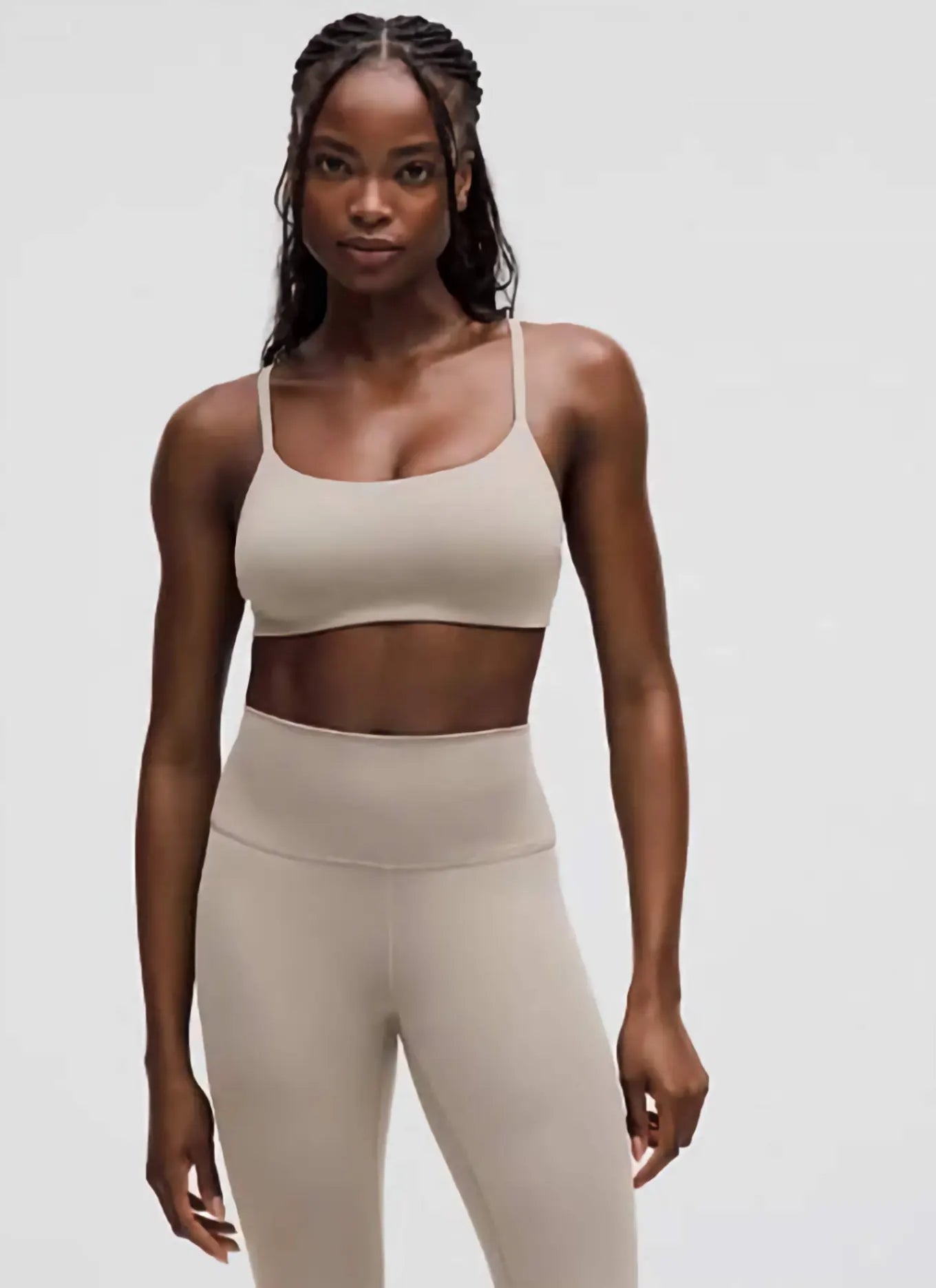 Woman wearing a beige sports bra and leggings on a plain background