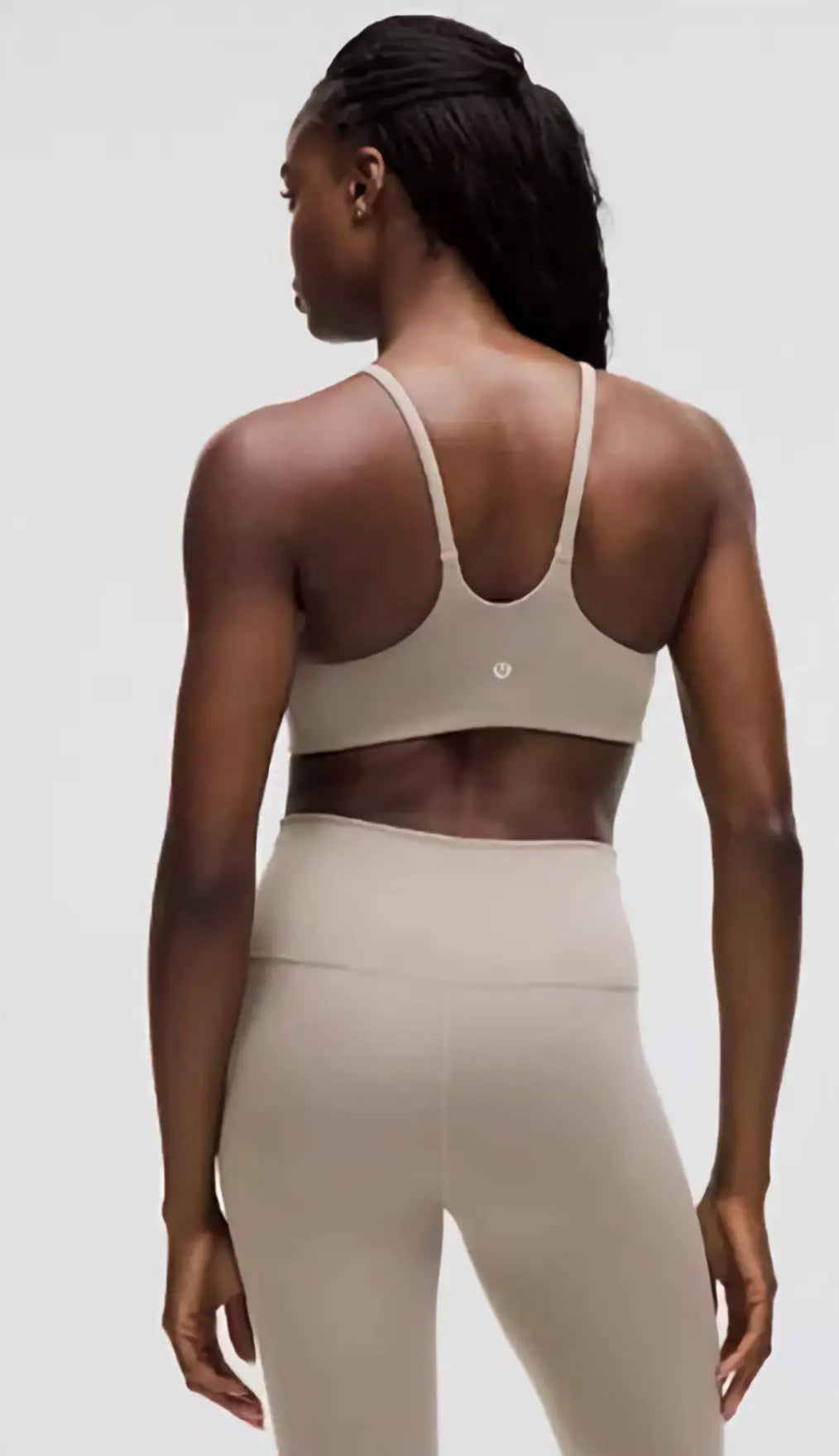 Person wearing a beige sports bra and leggings on a plain background